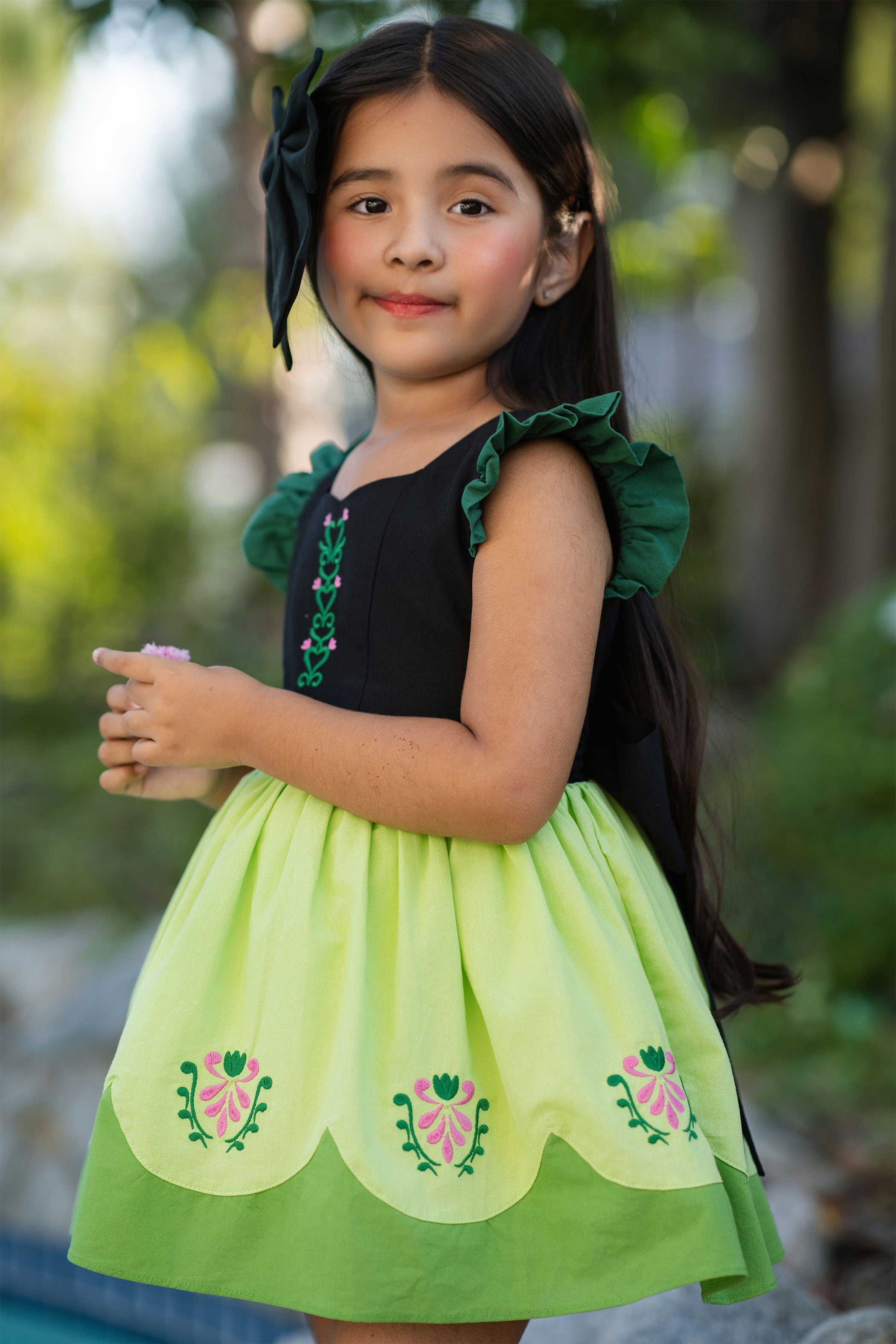 Young girl wearing a green and black dress with floral patterns outdoors.