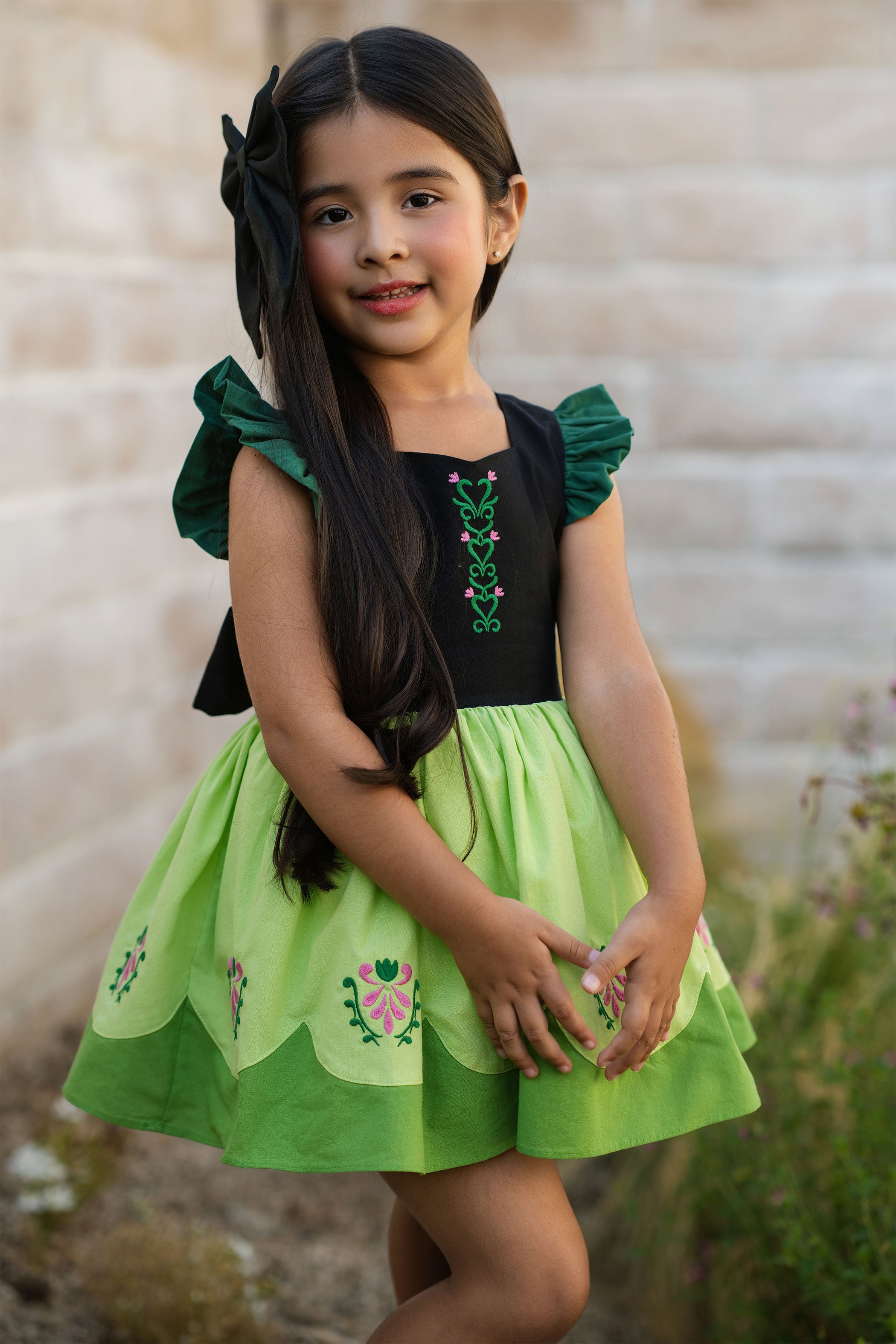 Young girl wearing a green and black dress with floral embroidery outdoors.