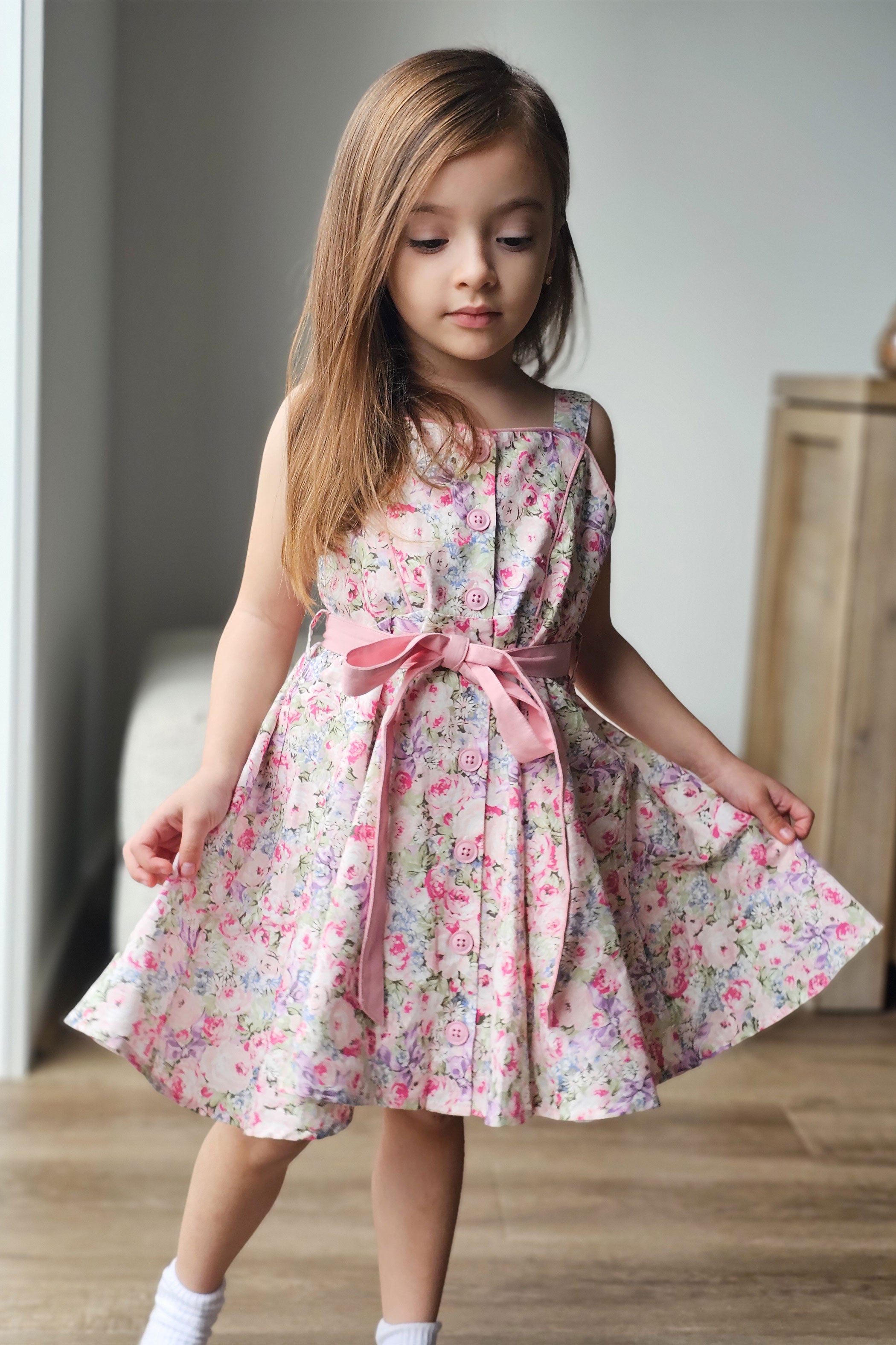 Young girl wearing a floral dress with a pink ribbon in a neutral setting