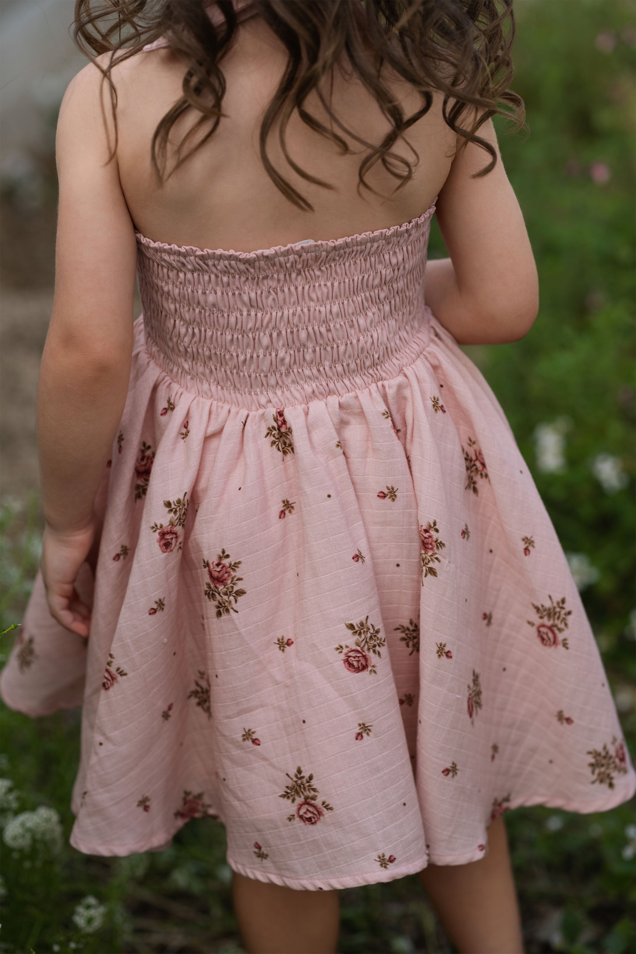 Child wearing a pink floral dress standing in a natural setting