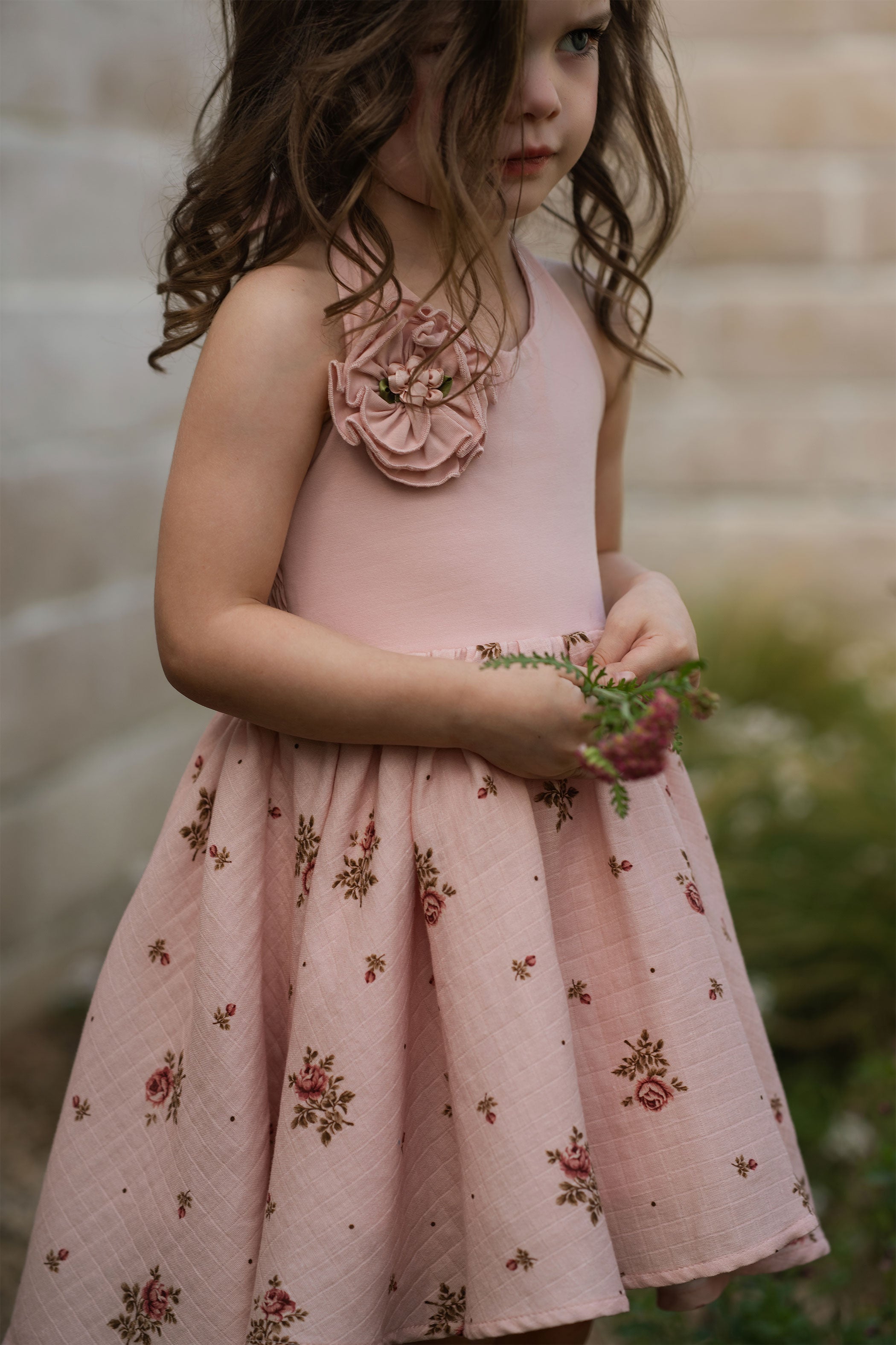 Young girl in a pink floral dress holding flowers outdoors.
