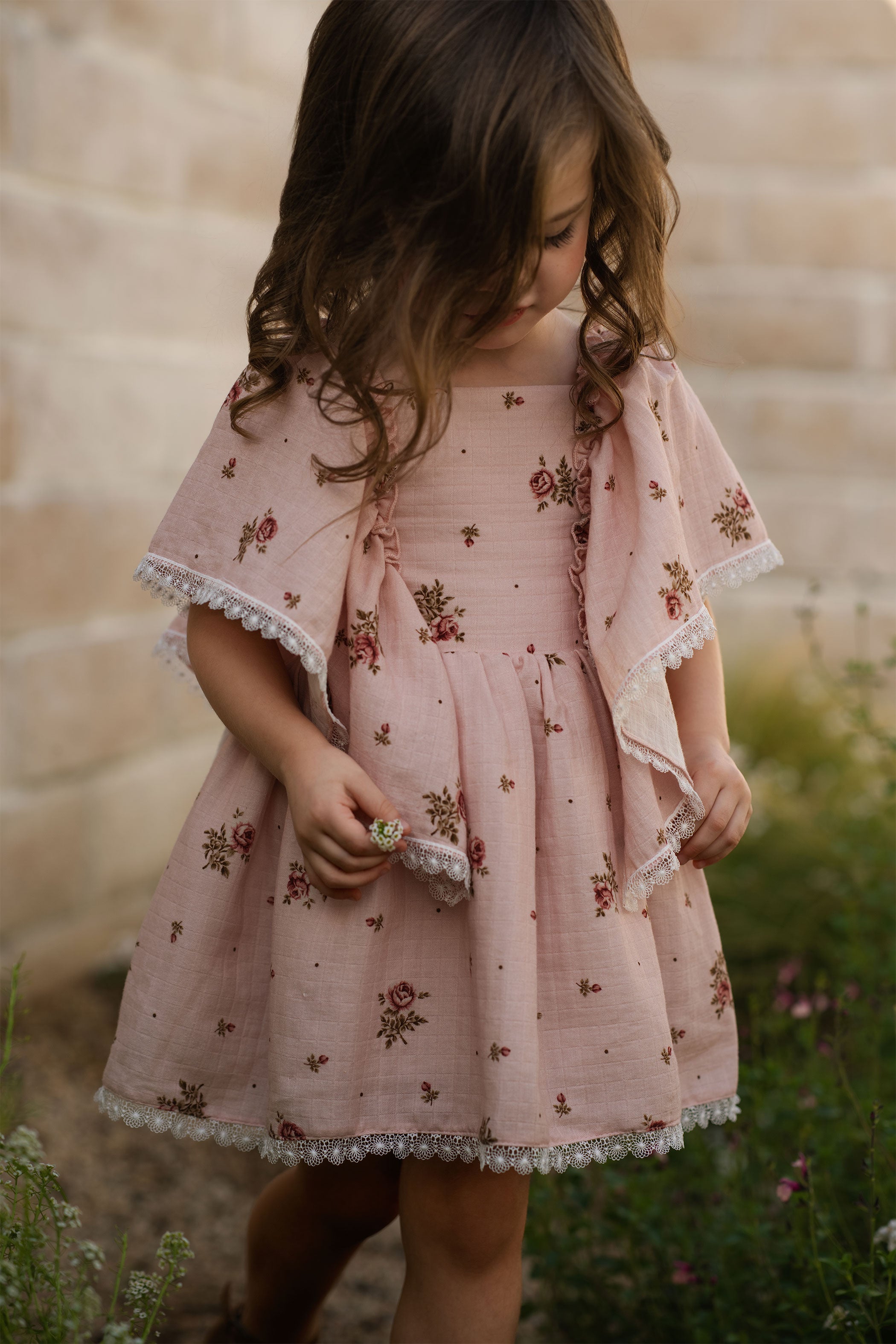 Young girl wearing a pink floral dress standing outdoors with a blurred background