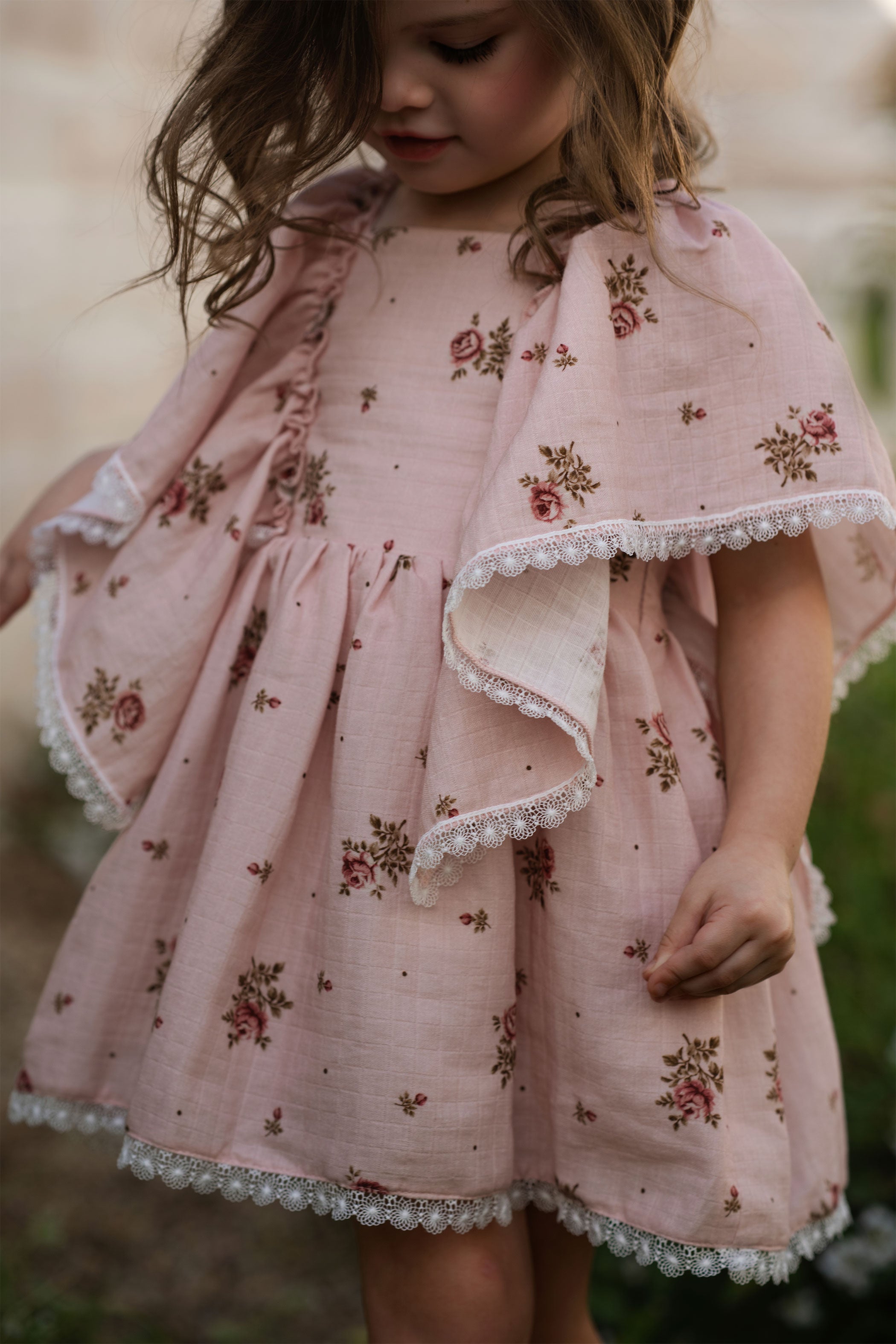 Child wearing a pink floral dress with ruffled sleeves and hem.