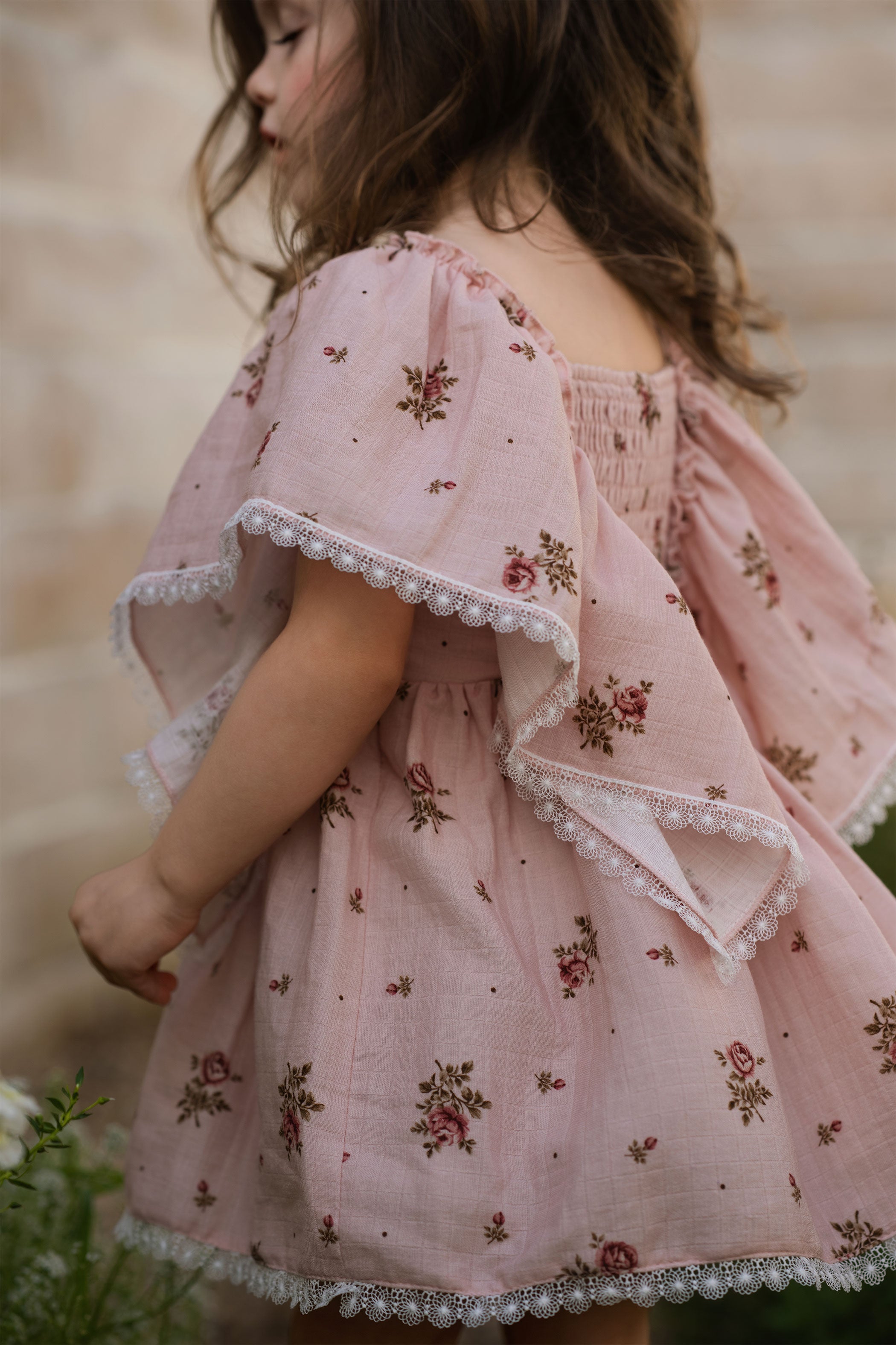 Child wearing a pink floral dress with ruffled sleeves against a blurred natural background