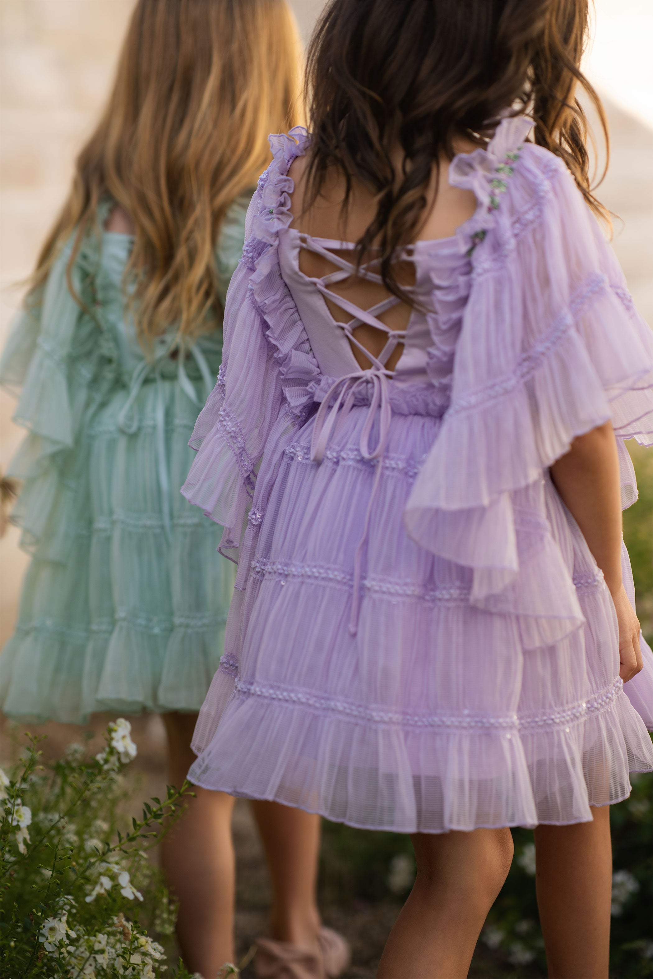 Two children wearing dresses in a natural setting with blurred background