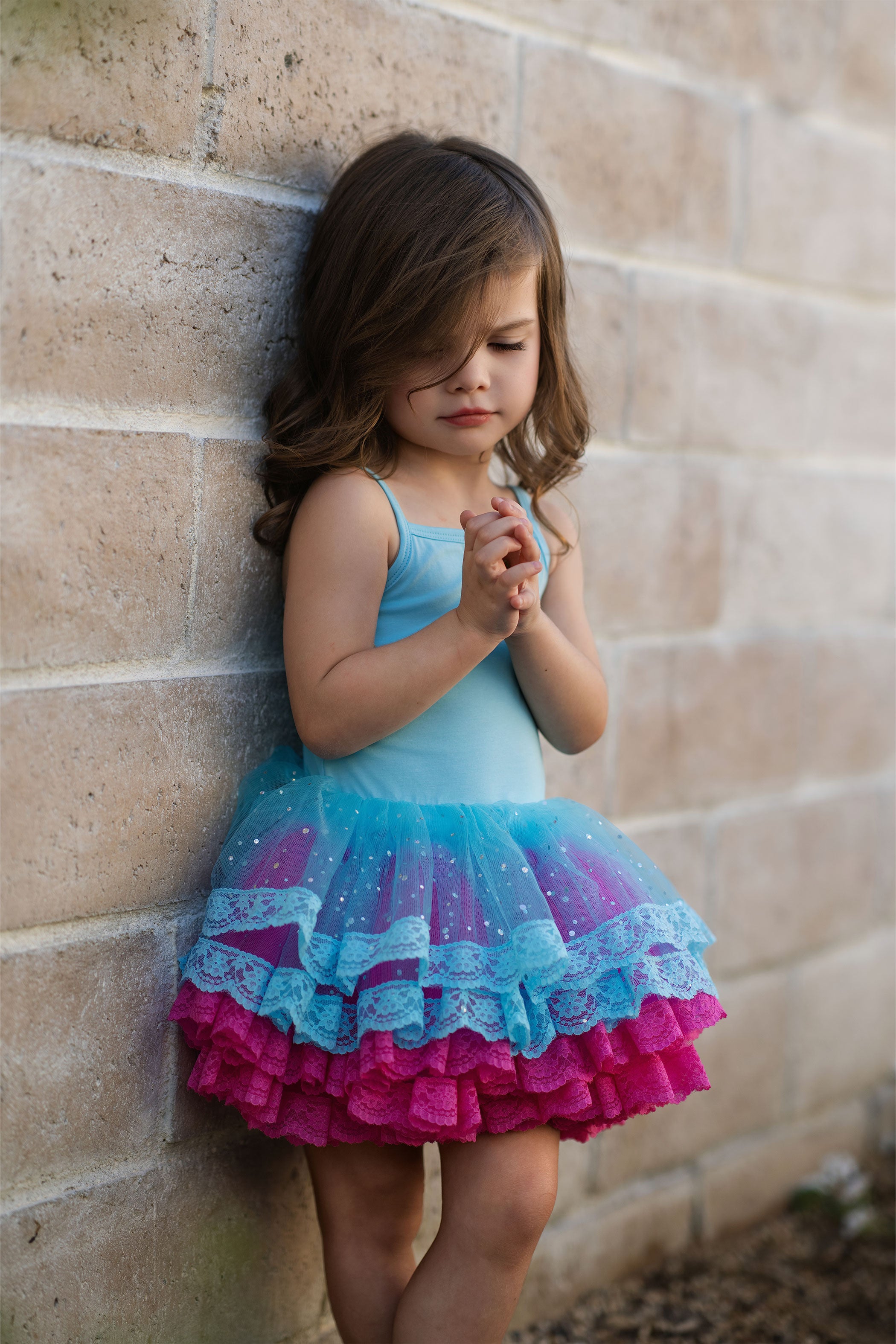 Young girl wearing a colorful dress against a brick wall